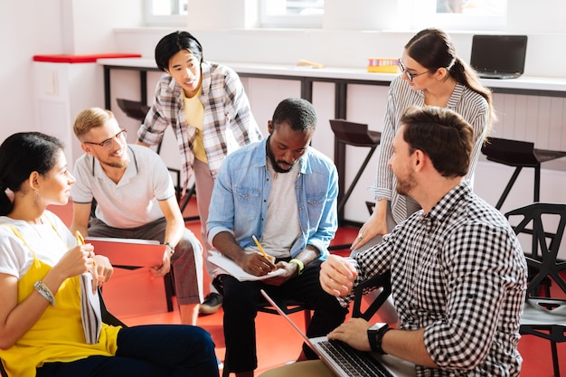 Foto tomando notas. tranquilo y concentrado profesor joven sosteniendo un lápiz y escribiendo las mejores ideas de su inteligente grupo de estudiantes mientras las escucha