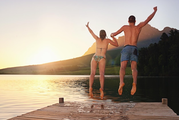 Tomando o mergulho foto retrovisor de um jovem casal em trajes de banho pulando de uma doca ao pôr do sol