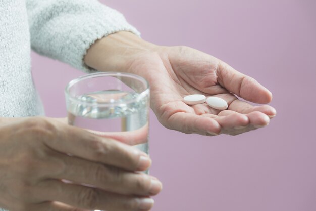 Tomando pastillas de medicina. La mujer sostiene en las manos las píldoras de la medicina y un vaso de agua.