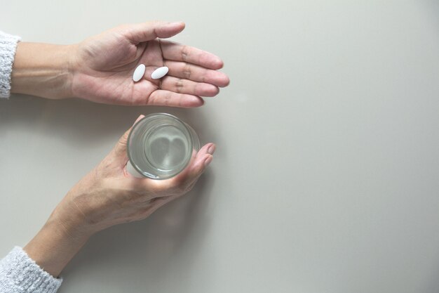 Tomando pastillas de medicina. La mujer sostiene en las manos las píldoras de la medicina y un vaso de agua.