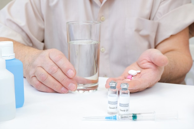 Tomando pastillas, un vaso de agua en la mano de una persona mayor. Vacunación de una persona adulta en un hospital. Concepto de salud, vacuna contra el coronavirus.