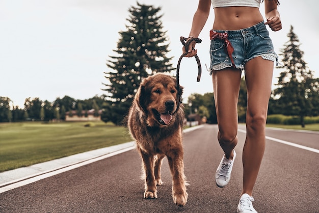 Tomando un poco de aire fresco. Primer plano de mujer joven corriendo con su perro por el parque mientras pasa tiempo al aire libre