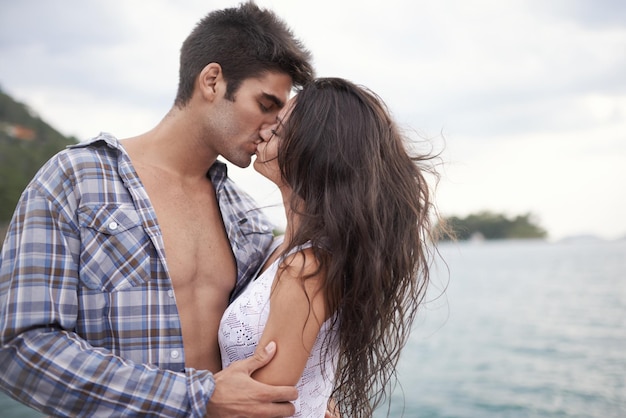 Tomando su amor afuera Foto de una joven pareja íntima disfrutando de un beso al borde del agua