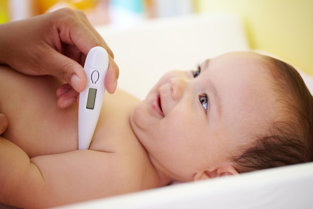 Tomando su temperatura Una niña sonriente mirando hacia arriba mientras su madre le toma la temperatura