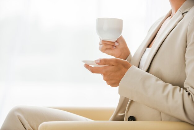 Tomando tiempo para la pausa para el café. Vista lateral de la empresaria en traje tomando café y mirando a otro lado mientras está sentado en la silla