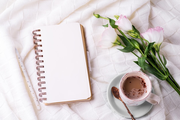 Tomando uma xícara de café, flores eustoma e notebook no cobertor na cama.