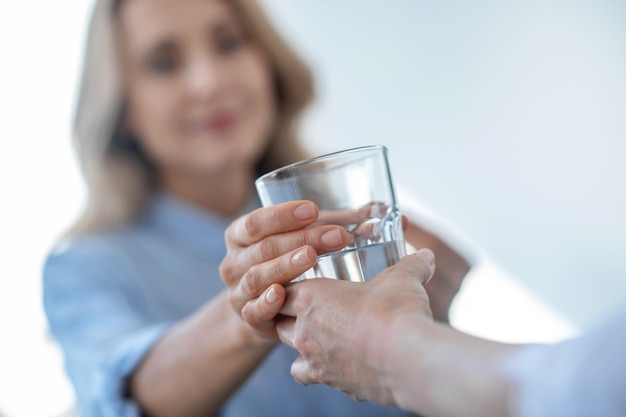 Tomar medicamentos. Primer plano de manos femeninas dando un vaso de agua a la mujer rubia