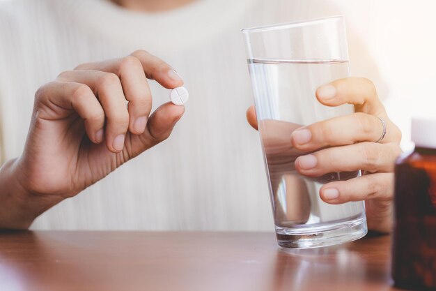 Foto tomar uma pílula e beber água com a garrafa marrom na mesa para o conceito de cuidados de saúde