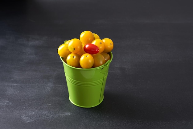 Tomate cereja amarelo em um mini balde verde sobre um fundo escuro.