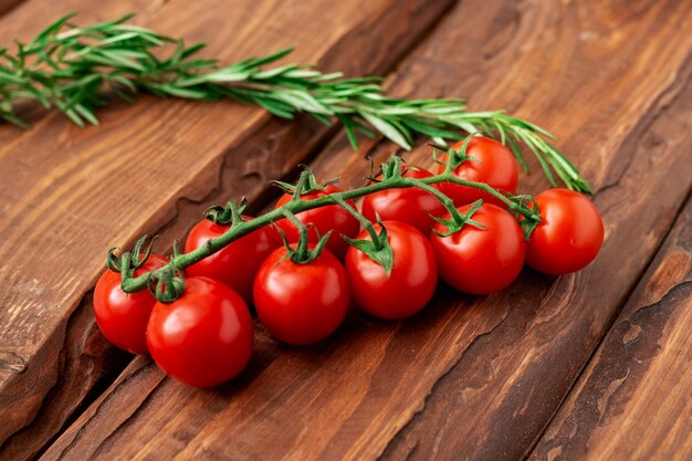 Tomate cereja e alecrim em um fundo de madeira. Ramo de tomate fresco. Comida vegetariana.