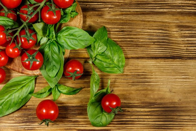 Tomate cereja fresco com folhas de manjericão verde em uma mesa de madeira Vista superior