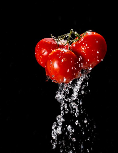 Tomate cereja recebendo respingos de água no fundo preto.