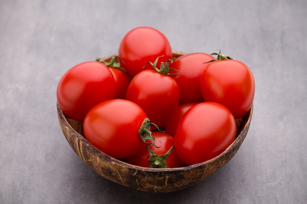 Tomate cereja. Três tomates cereja em uma tigela de madeira sobre uma mesa cinza