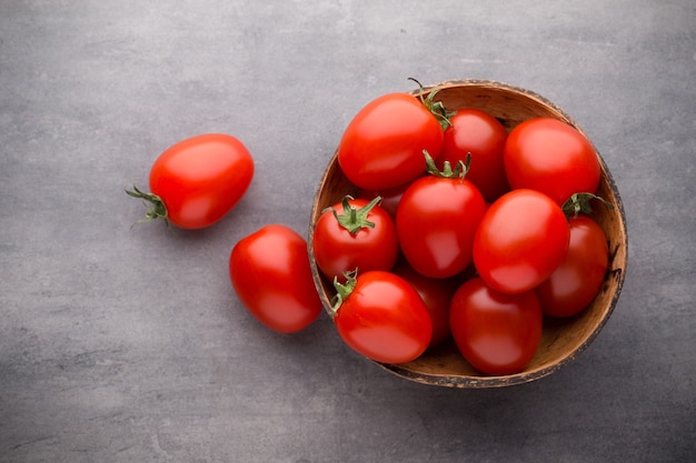 Tomate cereja. Três tomates cereja em uma tigela de madeira sobre uma superfície cinza.