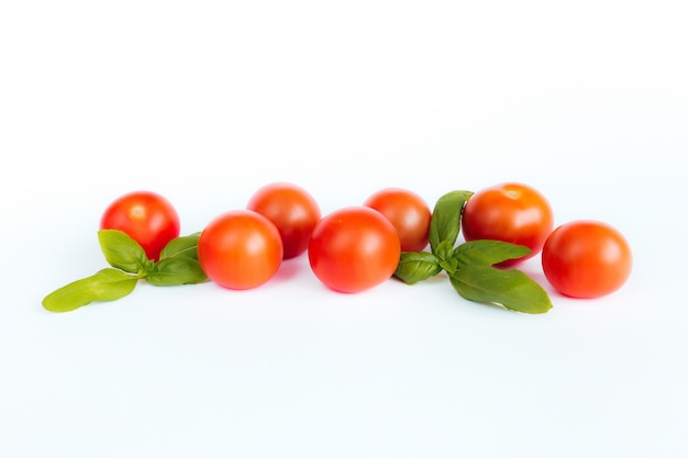 Tomate cereja vermelho com manjericão verde em uma superfície branca.