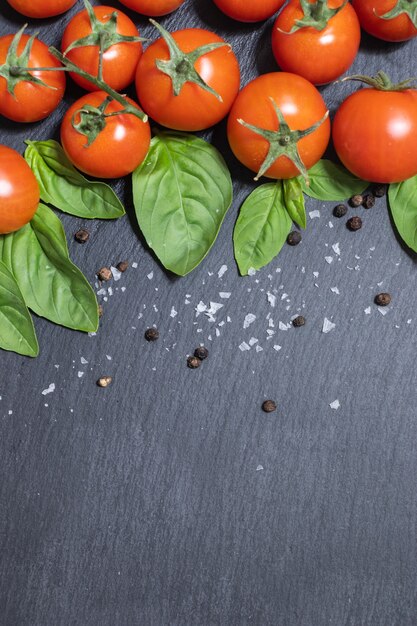 Tomate cereja vermelho fresco cru em fundo escuro com manjericão e alho