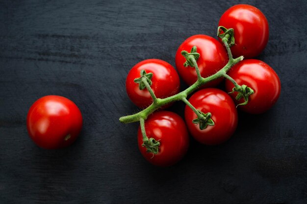 Tomate cereja vermelho sobre fundo preto de madeira. Legumes orgânicos maduros frescos com pedúnculos closeup o