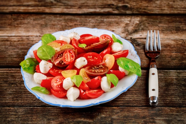 Tomate cherry con queso mozzarella en plato blanco con tenedor. De cerca.