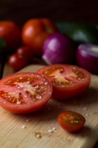 El tomate cortado por la mitad se espolvorea con grandes trozos de sal en una tabla de cortar de una variedad de vegetales coloridos.