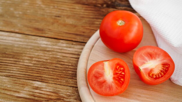 Foto tomate entero y cortado sobre una tabla de madera para rebanar y fondo de madera