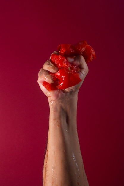 Tomate esmagado por mão masculina em fundo vermelho