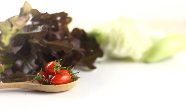 Tomate fresco en la cuchara de madera contra el fondo de las verduras de la falta de definición