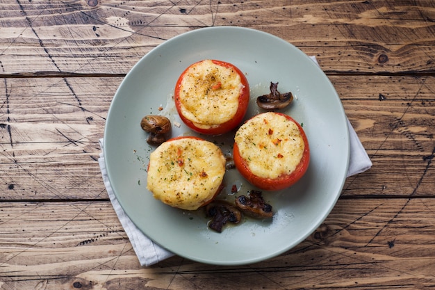 Tomate inteiro assado recheado com cogumelos e queijo com temperos em uma mesa de madeira. Copie o espaço.