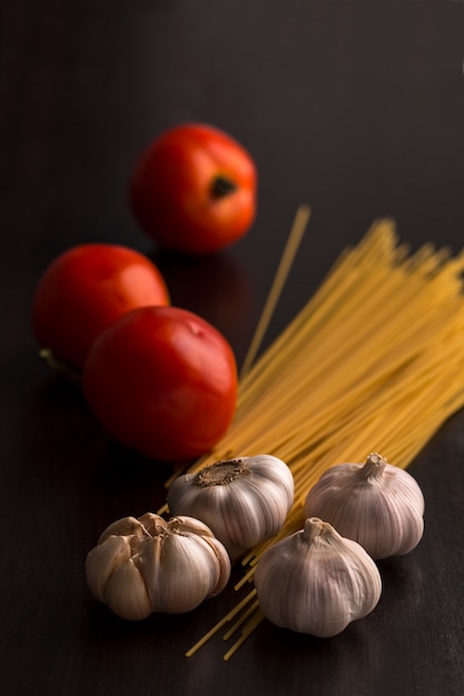 Tomate, Knoblauch und rohe Spaghettis auf Holz.