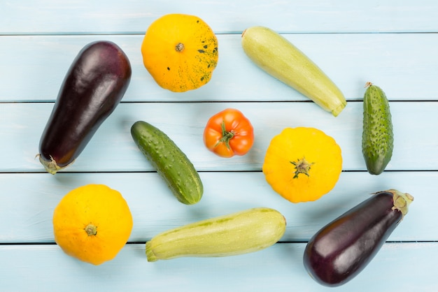 Tomate, pepino, arbusto de calabazas, berenjenas y calabacines en mesa de madera azul.