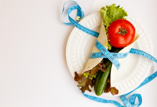 Tomate, pepino, salade vive no prato, fita métrica azul enrolada em torno de pão sírio em um fundo branco, perda de peso e estilo de vida adequado, conceito de dieta, espaço de cópia