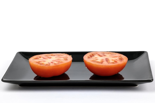 Tomate en plato negro aislado sobre fondo blanco.