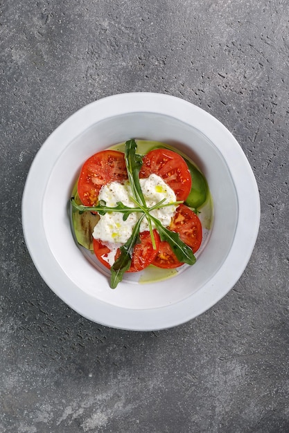 Tomate con queso ricotta en plato blanco sobre fondo de hormigón gris