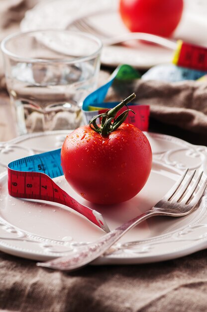 Tomate rojo, cinta métrica y agua.