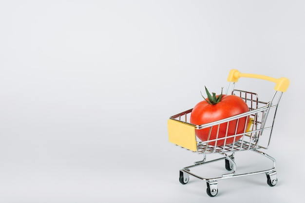 Tomate rojo jugoso en carrito de compras sobre fondo blanco