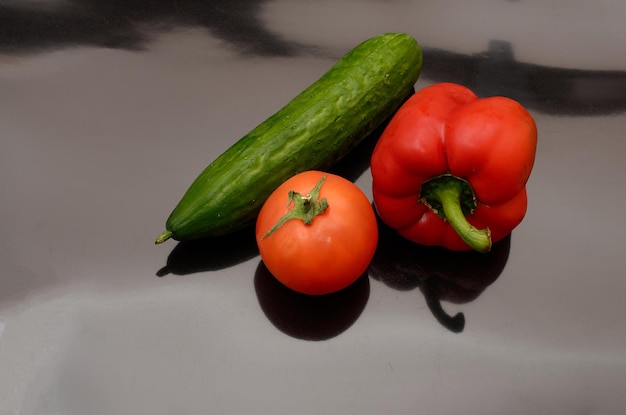 Un tomate rojo y un pepino sobre una superficie negra.