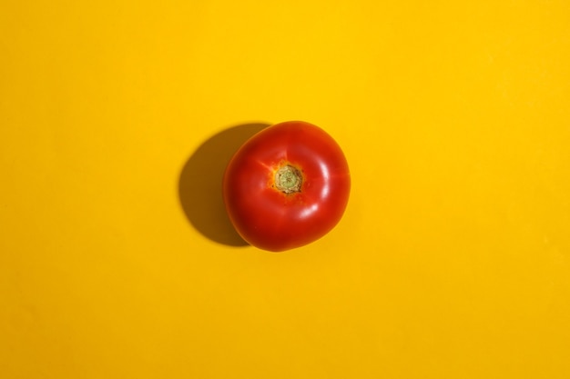 Tomate rojo sobre fondo amarillo brillante.