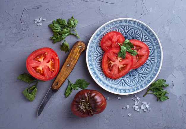 Tomate, sal, perejil y cuchillo en el fondo concreto gris. Enfoque selectivo, vista superior