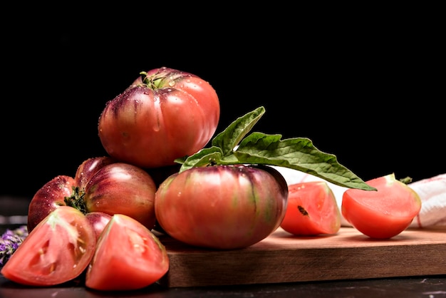 Tomate tigre en una tabla de cortar con hojas de albahaca sobre fondo de madera Espacio de copia Tomate fresco para cocinar Tomate con gotas de agua