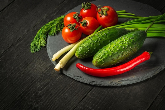 Tomate vermelho e cebolinha verde com pepino em uma placa preta