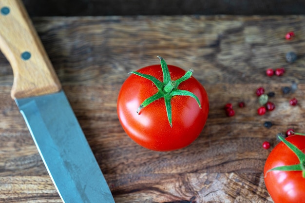 Foto tomate vermelho e faca de cozinha em uma tábua de madeira escura