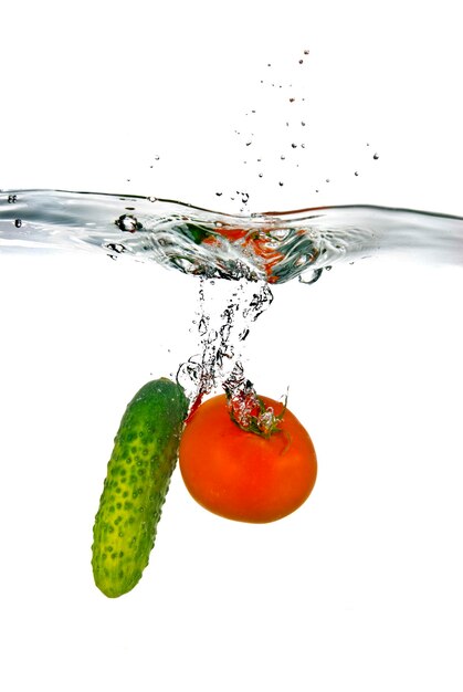 Foto tomate vermelho e pepino verde jogados na água isolado no branco