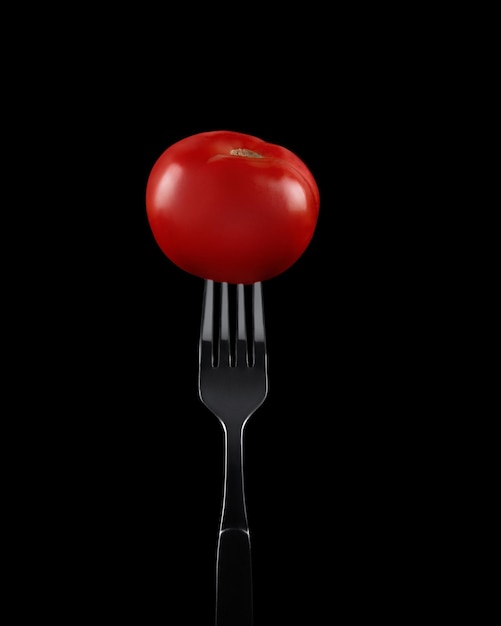 tomate vermelho em um garfo em um fundo preto