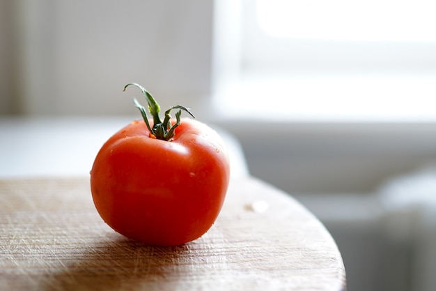 Tomate vermelho em uma placa de madeira de corte no fundo branco.