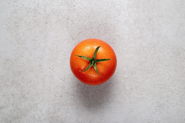 Tomate vermelho fresco com gotas de água em uma pedra cinza. Fundo para receitas.