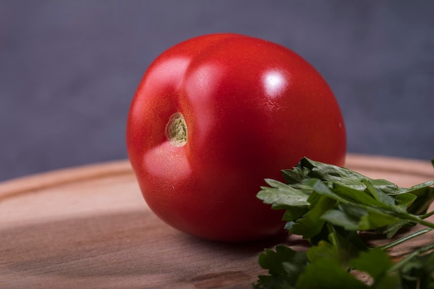 Tomate vermelho suculento com um raminho de salsa closeup em cima da mesa