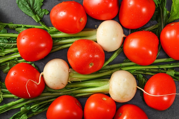 Foto tomate vermelho vibrante e raízes de rabanete branco com folhas verdes em mesa cinza escuro vista de cima conceito de vegetais saudáveis