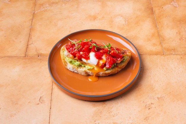 Tomaten-Bruschetta mit Avocado-Guacamole-Basilikum und Olivenöl auf brauner runder Keramikplatte serviert ...