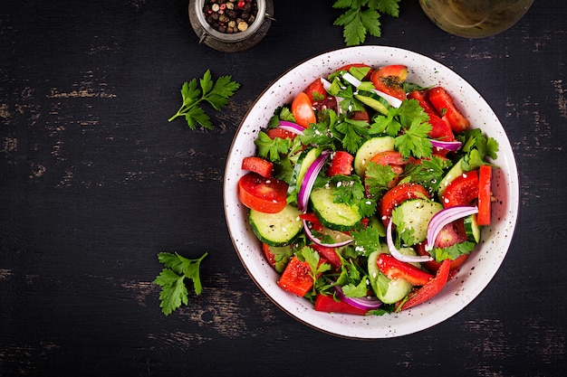 Tomaten-Gurken-Salat mit roter Zwiebel, Paprika, schwarzem Pfeffer und Petersilie. Veganes Essen. Diät-Menü. Ansicht von oben. Flach liegen