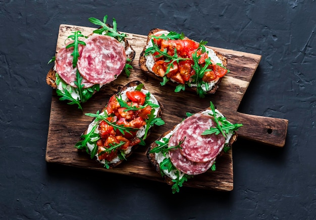 Tomaten italienische Wurst und Rucola Vollkornbrot Bruschetta auf einem Schneidebrett aus Holz