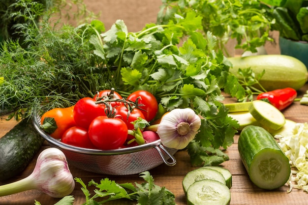 Tomaten, Knoblauch und Gemüse im Sieb. Geschnittene Gurken und Kohl auf dem Tisch. Hölzerner Hintergrund.